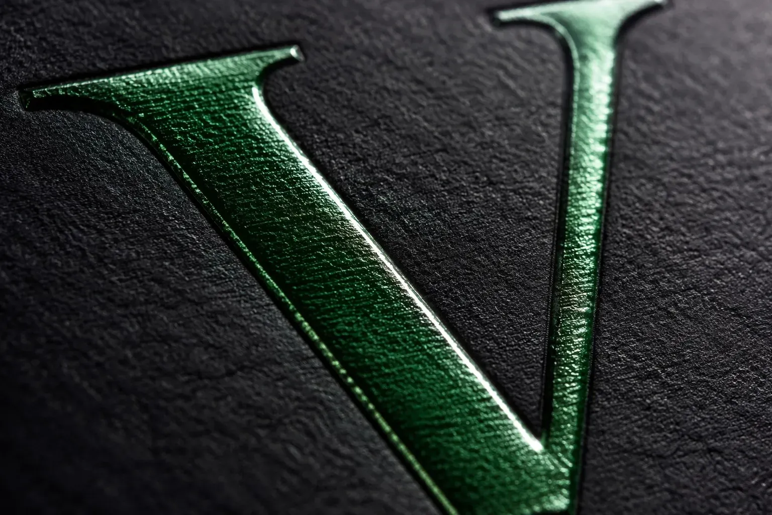 Green foil serif V embossed on black textured paper — brand identity craft