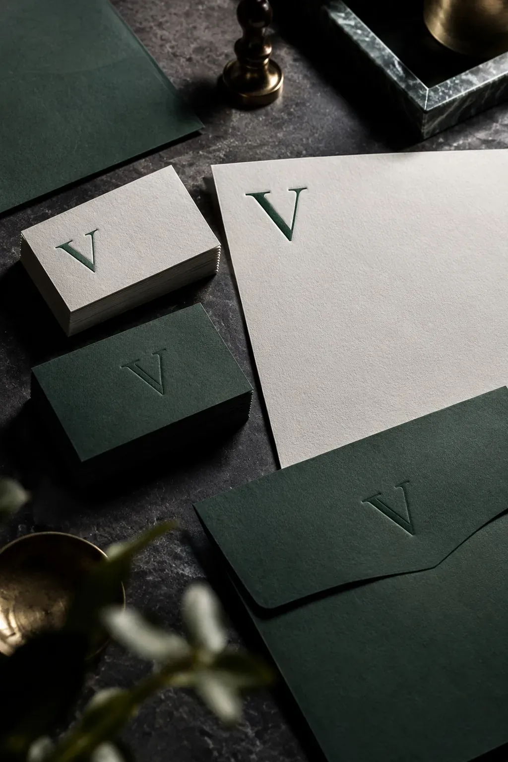 Premium printed brand stationery with an embossed green serif V logo on a dark stone desk — brand identity at Veles Labs